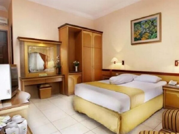 Une chambre d’hôtel comprenant un lit, un bureau, une armoire, un miroir, une table de chevet et un tableau au mur.