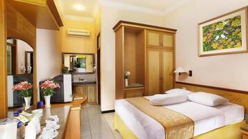 A hotel room with a bed, a desk with a computer, a wardrobe, and a painting on the wall.