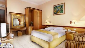 A hotel room with a bed, a desk with a computer, a chair, a wardrobe, and a painting on the wall.