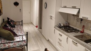 Une cuisine de taille réduite avec des meubles blancs, une cuisinière à gaz et un évier. La pièce adjacente contient un lit avec une literie à motifs floraux.