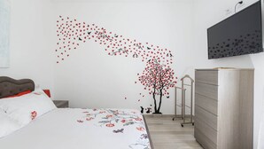Une chambre à coucher avec un lit, une commode et un motif décoratif représentant un arbre avec des cœurs sur un mur.