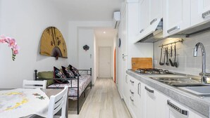 Une cuisine de taille réduite avec des meubles blancs, un évier en acier inoxydable et une planche à découper en bois.