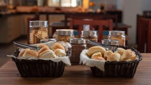 A table with baskets of bread rolls and jars of condiments in a restaurant setting. - Hotel Ciribai Maceio (Maceió)
