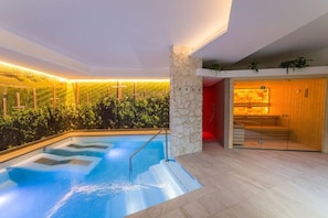 Un espace piscine intérieur moderne, agrémenté d’une colonne en pierre, d’un escalier en bois et offrant une vue sur un vignoble.