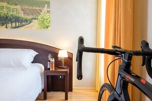 Une chambre d’hôtel avec un lit, une table de chevet avec une lampe, un vélo et un tableau représentant des vignes accroché au mur.