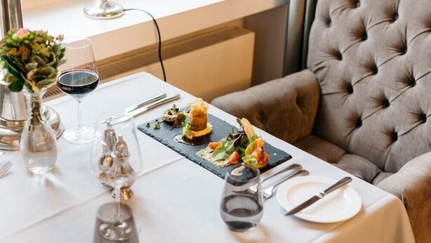 Une table à manger dressée avec une assiette en ardoise noire, des verres à vin et des couverts.