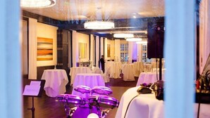 Une salle de bal d’hôtel avec des tables dressées pour des événements, une scène avec des instruments de musique et un grand lustre.