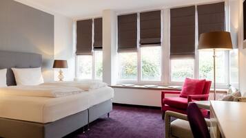 Ein Hotelzimmer mit Bett, Schreibtisch, Stuhl und großen Fenstern mit Jalousien.