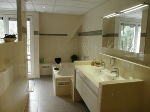 A modern bathroom with a bathtub, a large mirror, and a sink. - Westcord Hotel de Veluwe (Garderen)