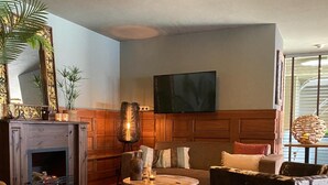 Un salón acogedor con chimenea, una mesa de centro redonda, un sofá y un televisor montado en la pared.