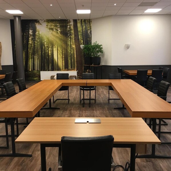 A conference room with a long table, black chairs, a plant, and a forest mural on the wall.