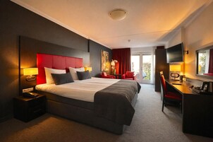 Habitación de hotel con una cama grande, un escritorio, una silla, un televisor y un cuadro en la pared.
