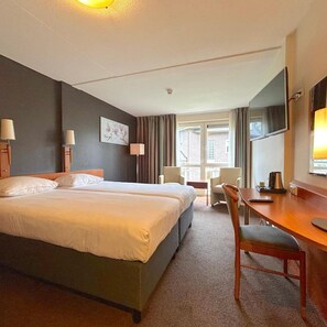 A hotel room with a bed, two bedside tables, a desk, a chair, a TV, and a window with curtains. - Westcord Hotel de Veluwe (Garderen)