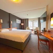 A hotel room with a bed, two bedside tables, a desk, a chair, a TV, and a window with curtains.