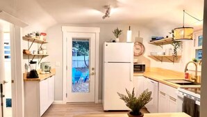 Eine kleine Küche mit weißen Schränken, einer Holz Arbeitsplatte, einem Kühlschrank, einer Mikrowelle und einem Topfpflanzen.