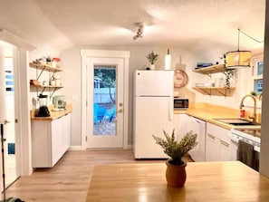 Eine kleine Küche mit weißen Schränken, einer Holz Arbeitsplatte, einem Kühlschrank, einer Mikrowelle und einem Topfpflanzen.