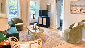 Ein Wohnzimmer mit Sofa, Sessel, Couchtisch, Fernseher und einem Gemälde an der Wand.