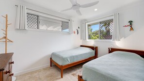 A bedroom with two single beds, a ceiling fan, and a window with a view of greenery. - Currimundi Retreat Pet Friendly, Walk to the beach (Battery Hill)