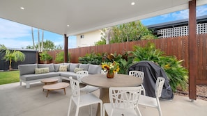 An outdoor patio with a grey sectional sofa, white chairs, a round table, and a grill. - Currimundi Retreat Pet Friendly, Walk to the beach (Battery Hill)