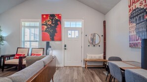 A modern living room with a high ceiling, a sofa, a dining table, and a large abstract painting. - The Jazzy Junction-Great Downtown Location! (Pensacola)