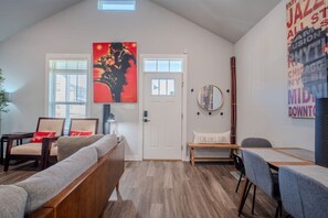 Ein modernes Wohnzimmer mit hohen Decken, einer Couch, einem Esstisch und einem großen abstrakten Gemälde.