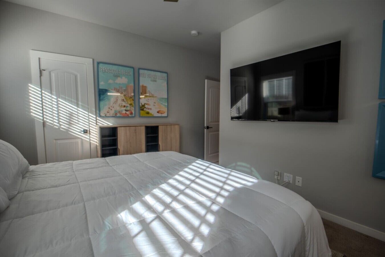 A bedroom with a bed, a TV mounted on the wall, and two doors.
