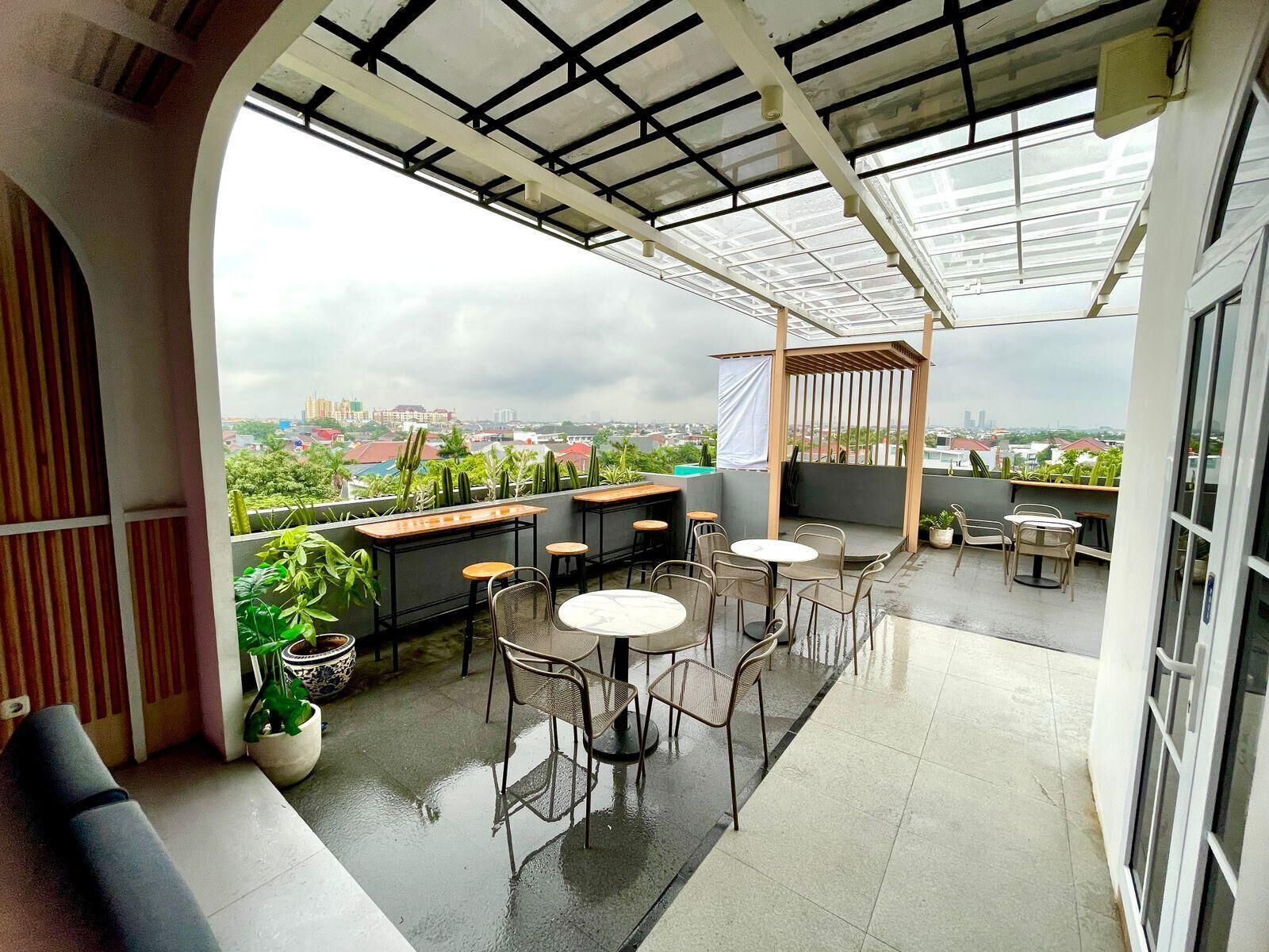 A rooftop terrace with a view of the city, featuring outdoor seating and potted plants.