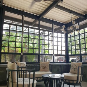 Una habitación con techo alto, ventanas grandes con diseño de cuadrícula y una mesa redonda con sillas.