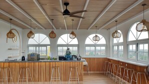 Un espacio amplio para bar con detalles de madera, ventanas arqueadas grandes y lámparas de mimbre colgantes.