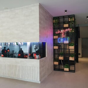 Un área de recepción con un letrero de neón que dice 'chee & CHILL' y una estantería con plantas.