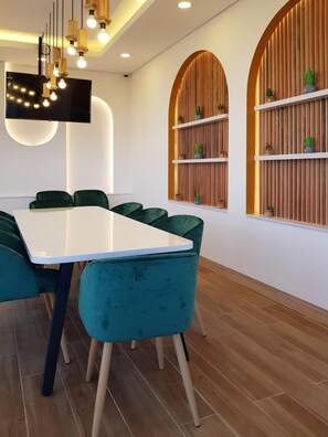 Una sala de reuniones moderna con una mesa blanca, sillas color turquesa, estantes de madera con plantas e iluminación empotrada en el techo.