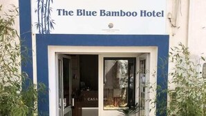 Entrada del Hotel Blue Bamboo con puerta de vidrio, plantas en macetas a cada lado y un letrero sobre la puerta.