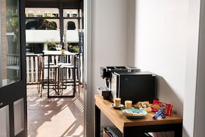 A room with a coffee machine, a table with a plate of food, and a window overlooking a balcony with chairs. - Holiday Inn West Perth (Perth)