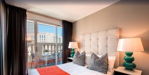 A hotel room with a large bed, two bedside lamps, a balcony with a view of buildings, and a red throw blanket. - Holiday Inn West Perth (Perth)