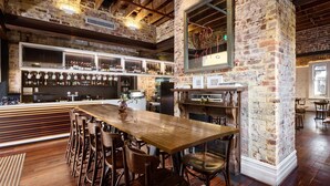 A bar area with a wooden bar counter, multiple stools, and a brick wall. - Holiday Inn West Perth (Perth)