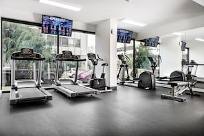 Un gimnasio con cintas de correr, elíptica y bicicleta estática, con ventanas amplias y televisores en las paredes.