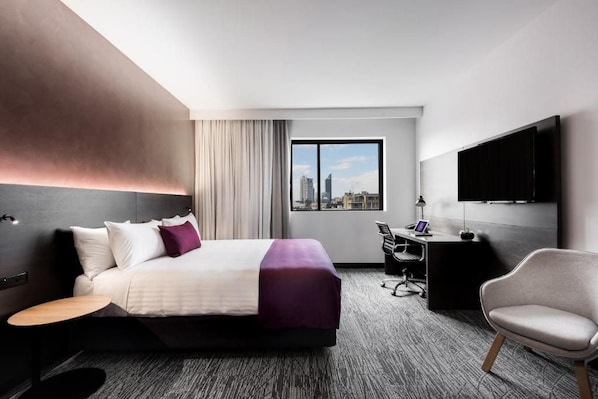 A hotel room with a bed, desk, chair, and a large window with a city view. - Holiday Inn West Perth (Perth)