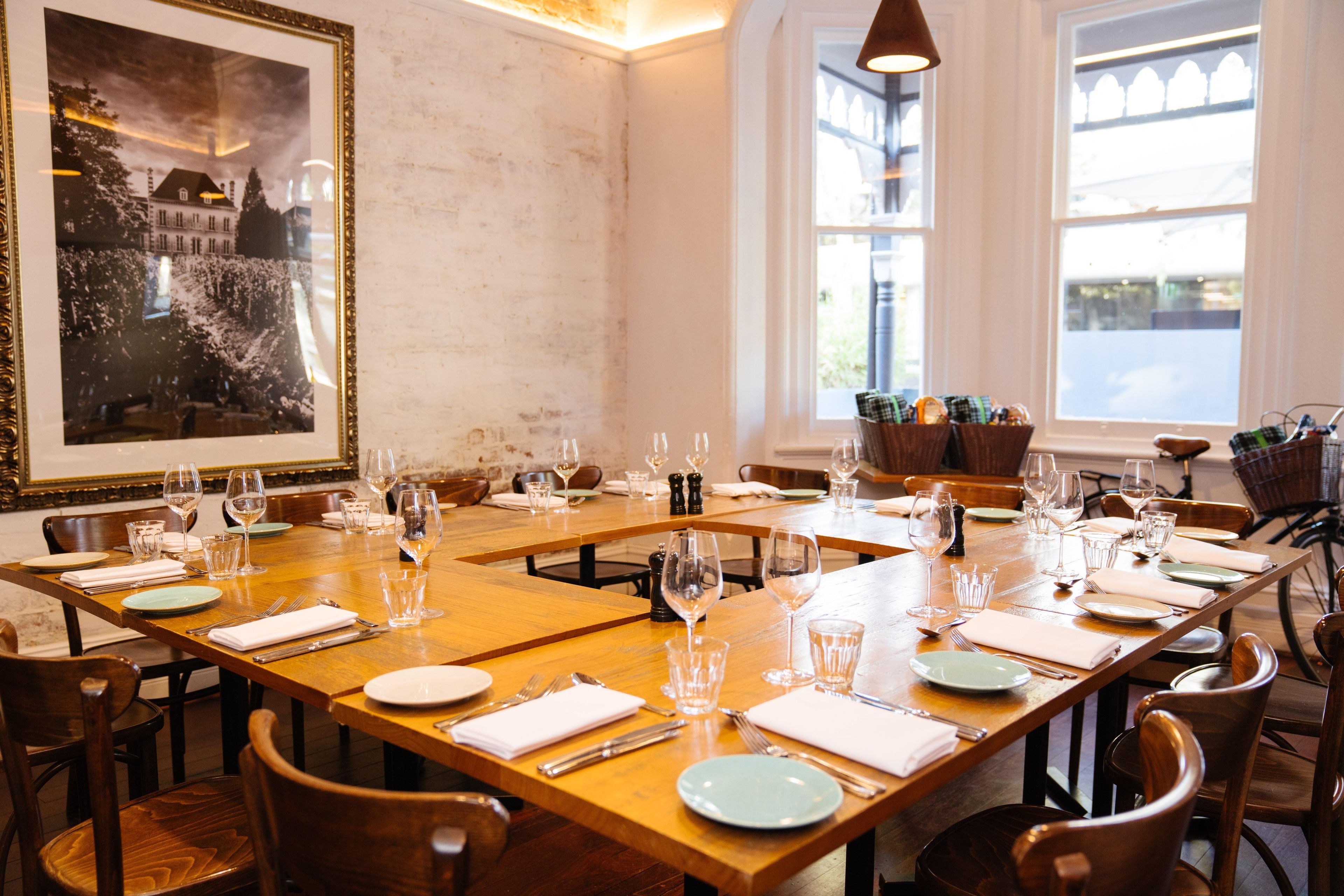 A dining area with wooden tables set for multiple guests, each table with plates, cutlery, and wine glasses.