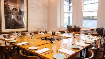 A dining area with wooden tables set for multiple guests, each table with plates, cutlery, and wine glasses.