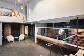 Un área de recepción moderna con mostrador, dos sillones blancos, una mesita y una escalera con barandilla metálica.
