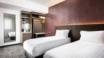 A hotel room with two beds, a wardrobe, a mirror, and a small table with a coffee maker.