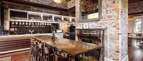 A bar area with a wooden bar counter, multiple stools, and a brick wall.