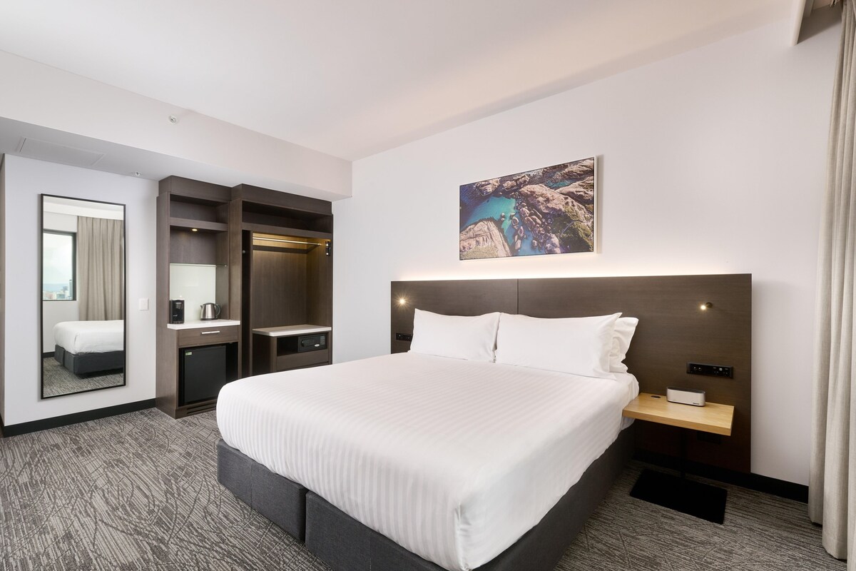 Una habitación de hotel con una cama grande, una mesita de noche, un armario y un cuadro en la pared.