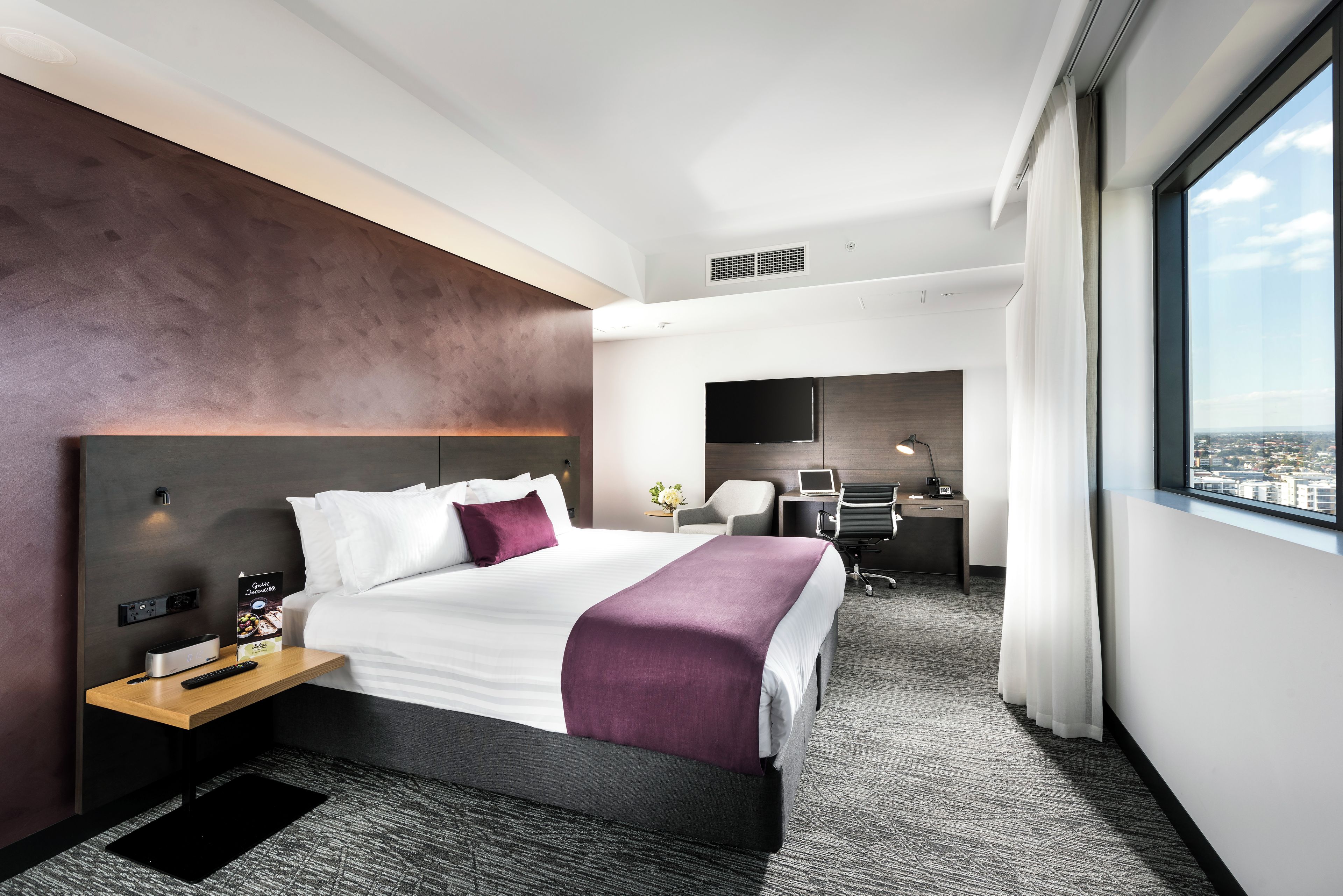 A modern hotel room with a large bed, a desk, and a view of the city.