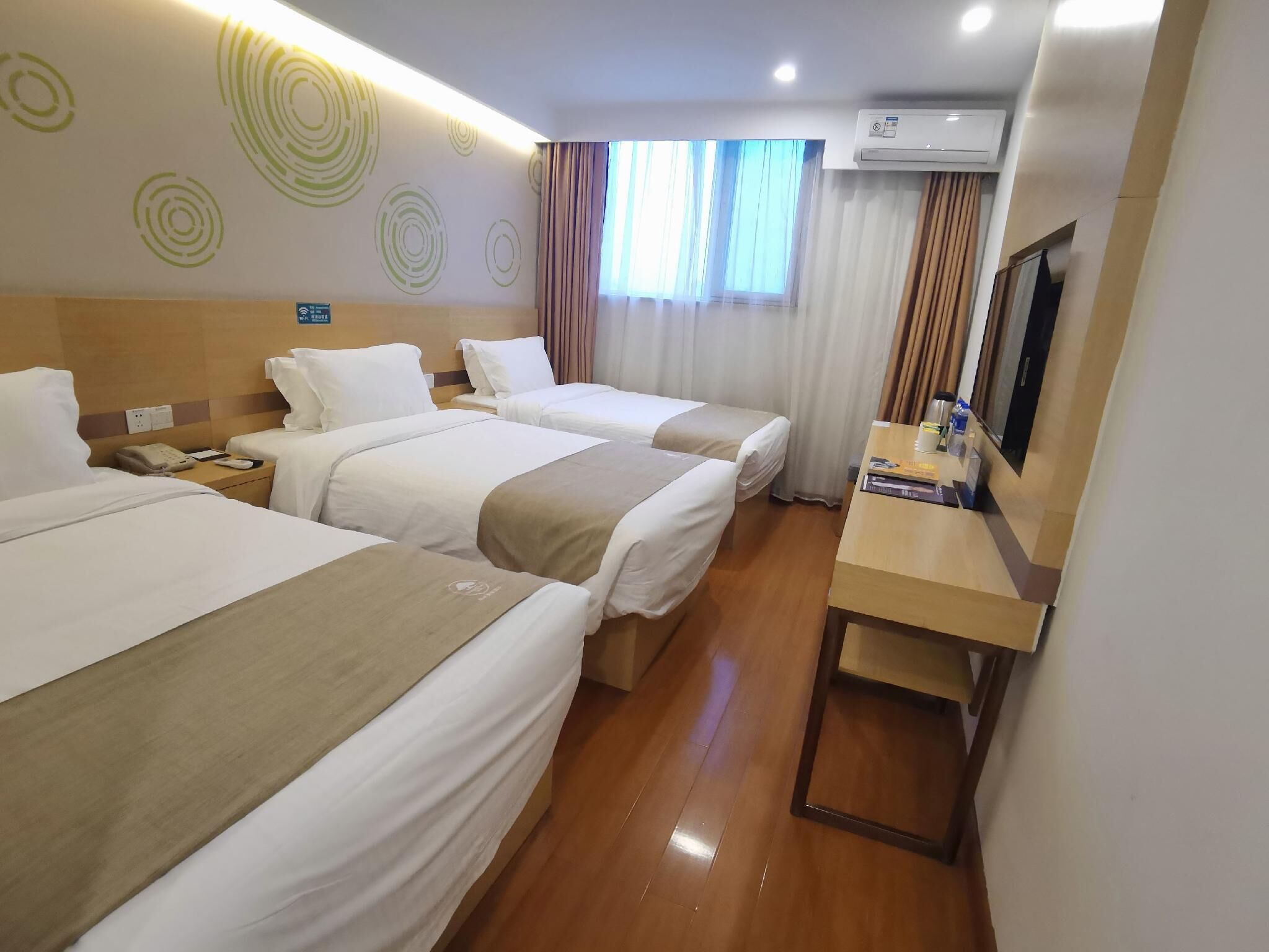 Une chambre d’hôtel avec deux lits, un bureau, un climatiseur et une fenêtre avec des rideaux.