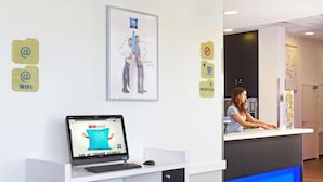 Zona de recepción con un mostrador, una computadora portátil mostrando un sitio web y una recepcionista.