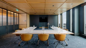 Un salón de conferencias con una larga mesa, sillas amarillas y ventanas amplias.