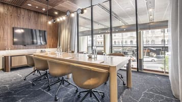 Uma sala de conferências com uma mesa comprida, cadeiras de couro, uma TV de tela plana e grandes janelas com vista para a cidade.