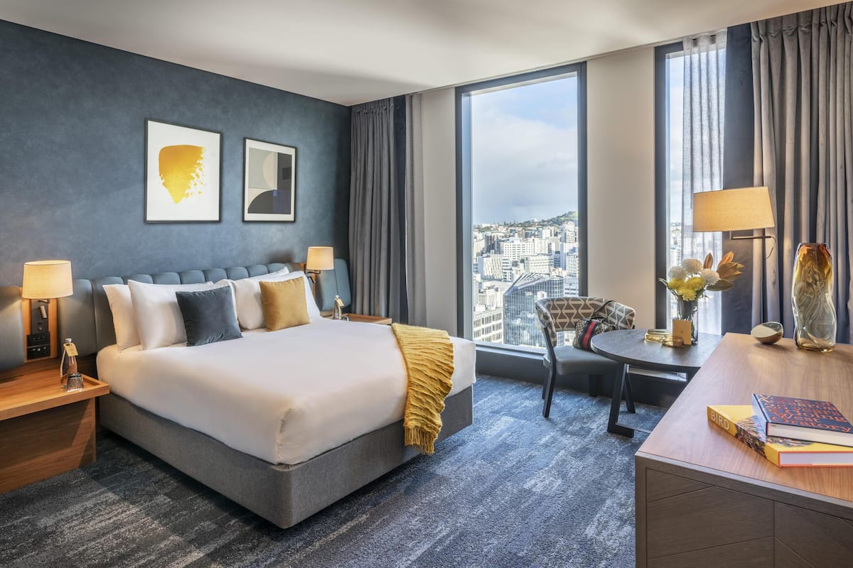 A hotel room with a large bed, a desk, a chair, and a view of the city.