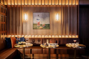 A modern interior with a wooden panel wall, a painting of a bottle and glasses, and a seating area with tables and cushions. - Voco Auckland City Centre (Auckland)